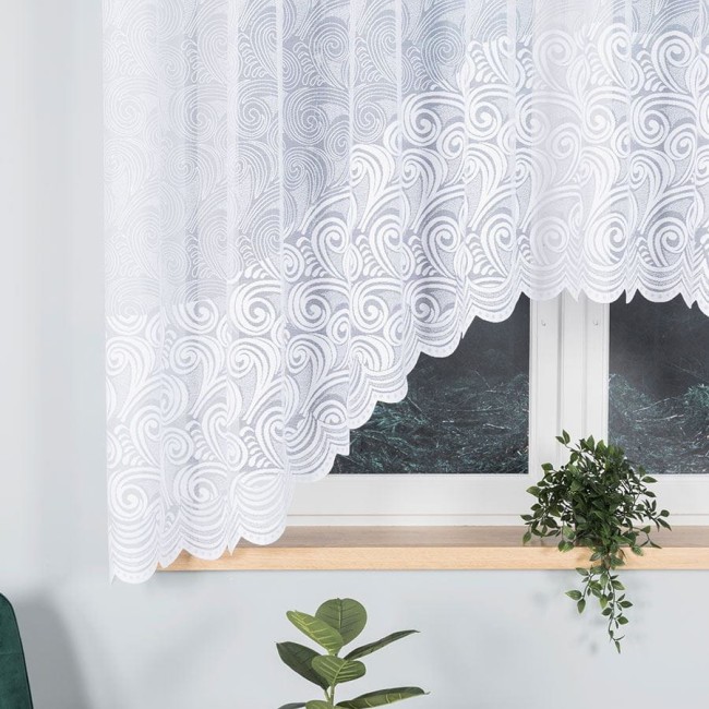 Firana żakardowa w kolorze białym o wymiarach 300x160 cm, z dekoracyjnym wzorem w kształcie spirali. Powieszona na oknie, z widoczną rośliną na parapecie oraz brązową ramą okna. Ujęcie frontalne. Tekstura lekka i przezroczysta.