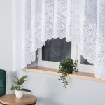 Firana gotowa Kinga żakardowa w kolorze białym, o wymiarach 300x160 cm, z falującym wzorem w formie spirali. Produkt wiszący na karniszu, umieszczony w kontekście okna, z rośliną doniczkową na parapecie. Tło w odcieniu szarym.
