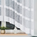 Firana gotowa Wiktoria żakardowa biała, o wymiarach 410x160 cm, zwisająca z okna. Materiał żakardowy z delikatnym, liniowym wzorem w białym odcieniu. Stojąca w zaaranżowanej przestrzeni z roślinnością w doniczce i lampionem na parapecie.