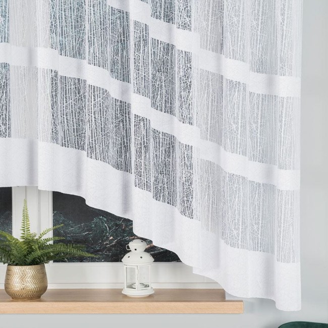Firana gotowa Wiktoria żakardowa biała, o wymiarach 410x160 cm, zwisająca z okna. Materiał żakardowy z delikatnym, liniowym wzorem w białym odcieniu. Stojąca w zaaranżowanej przestrzeni z roślinnością w doniczce i lampionem na parapecie.
