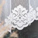 Firana gotowa Żaklina żakardowa w kolorze białym o wymiarach 400x160 cm, z ozdobnym, wysokiej jakości wzorem w kolorze białym i transparentnym materiale. Zbliżenie na dolną część firany, ukazujące dekoracyjny brzeg.
