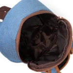 Otwarty pluszowy plecak dziecięcy z maskotką jednorożca, wykonany z błękitnego materiału zewnętrznego. Wnętrze w ciemnym kolorze, zapewniające dodatkową przestrzeń do przechowywania. Ujęcie z góry, z widoczną szaro-brązową taśmą zamka.