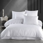 Pościel satyna bawełniana z gipiurą w kolorze białym 160x200, leżąca na łóżku. Widoczne wykończenia gipiury na poduszkach, zestaw składa się z kilku poduszek o różnych rozmiarach. Tło w ciemnym odcieniu podkreśla jasność pościeli.