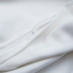 Zbliżenie na zamek błyskawiczny białej pościeli satynowej z gipiurą, rozłożonej na gładkiej powierzchni. Widoczne detale tkaniny oraz struktura materiału, ukazujące jego miękkość i gładkość. Brak dodatkowych dekoracji.