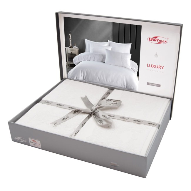 Pościel satyna bawełniana z gipiurą 160x200 Valinor w białym kolorze, zapakowana w szare pudełko z przezroczystym wiekiem. Zestaw zawiera poszewki i narzutę, ozdobiony delikatną wstążką. Widok z góry, na prosto ustawione elementy w estetycznym układzie.