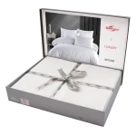 Pościel satyna bawełniana z gipiurą 220x200 Valinor w kolorze białym, zapakowana w eleganckie pudełko z szarym wiekiem i ozdobną kokardą. Widoczna grafika wewnątrz opakowania przedstawia komplet na łóżku. Zestaw zawiera poszwy na poduszki i kołdrę.