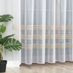 Firana żakardowa o wysokości 250 cm, przezroczysta, z delikatnymi złotymi paseczkami w poziomie. Produkt wiszący, widoczny obok zielonej rośliny w doniczce, na tle jasnej ściany.