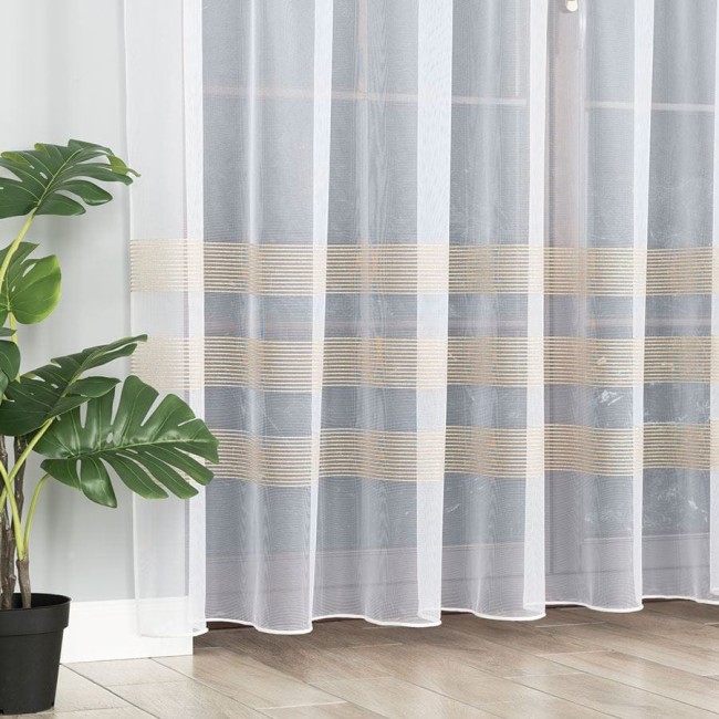 Firana żakardowa o wysokości 250 cm, przezroczysta, z delikatnymi złotymi paseczkami w poziomie. Produkt wiszący, widoczny obok zielonej rośliny w doniczce, na tle jasnej ściany.