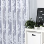Firana żakardowa w kolorze białym o wysokości 250 cm, z subtelnym, pełnym wzorem kwiatów, wisząca w pomieszczeniu. W tle widoczne doniczki z roślinami oraz dekoracyjna tablica. Tło białe, co podkreśla delikatność firany.