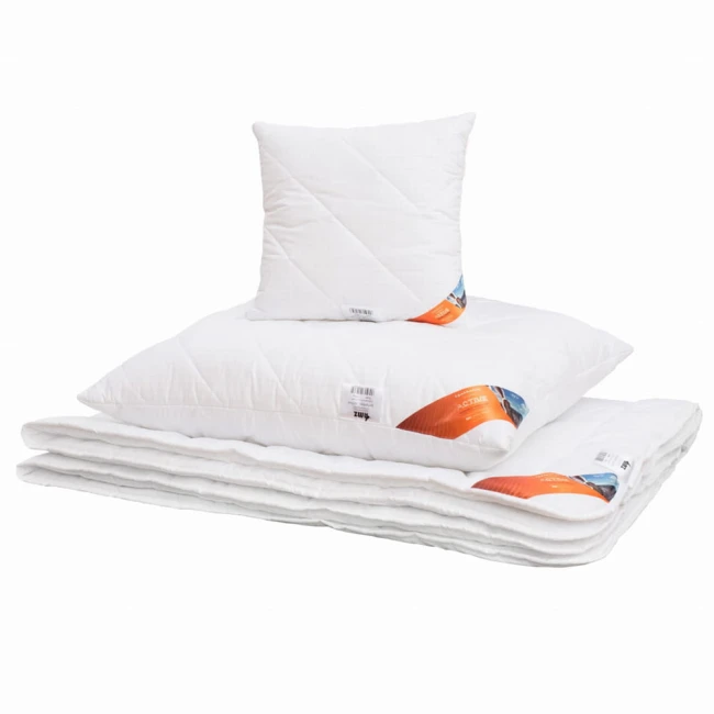 Kołdra całoroczna 155x200 cm w białym kolorze, antyalergiczna, z delikatną teksturą. Ułożona poziomo na białym tle, z widoczną poduszką w tle. Oznaczenie produktu w pomarańczowej etykiecie. W zestawie widoczny detal złożenia kołdry.