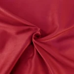Pościel satyna bawełniana w kolorze koralowym, rozłożona na gładkiej powierzchni, ukazuje miękką, lekko błyszczącą fakturę materiału. Widoczny detal to wyraźne zmięcie tkaniny, podkreślające jej elastyczność. Wymiary 140x200 cm.