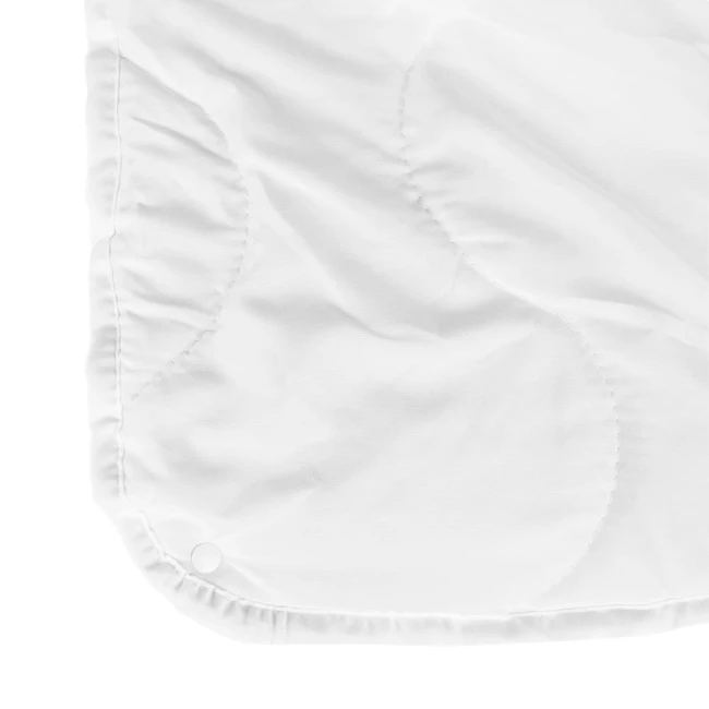 Biała kołdra antyalergiczna 200x220 cm, widoczna w zbliżeniu, z lekko teksturowanym materiałem. Zszycia tworzą delikatny wzór na wierzchu. Kołdra leży na płaskiej powierzchni, brzeg jest lekko falowany. Elementy mocujące są widoczne w rogach.