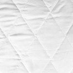 Biała poduszka antyalergiczna 50x70 klasyczny model, pikowana, z wyraźnym wzorem rombów. Wykonana z gładkiego materiału, z delikatnie błyszczącą powierzchnią. Zbliżenie na teksturę tkaniny, widoczny równomierny szew. Idealna do użytku domowego.
