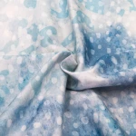 Pościel satynowa w odcieniach błękitu i bieli z wzorem w kropki, wykonana z bawełny, o wymiarach 220x200 cm. Materiał gładki i lekko błyszczący, złożony w zakładki na białym tle. Widoczne zbliżenie na fakturę tkaniny i wzór.