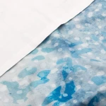 Pościel satyna bawełniana 220x200 Luxury Premium Belize w kolorze niebieskim i białym, z artystycznym wzorem w odcieniach błękitu, leżąca na płaskiej powierzchni. Widoczna biała poszewka na poduszkę oraz delikatnie teksturowana faktura.