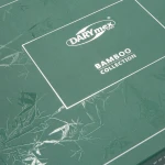 Beżowe opakowanie pościeli bambusowej, z widocznym logiem DARYmex i napisem Bamboo Collection. Tło w odcieniu ciemnozielonym, na którym widoczne są zarysy roślinności. Opakowanie ma prostokątny kształt oraz lekko teksturowaną powierzchnię.
