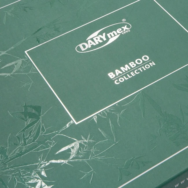 Beżowe opakowanie pościeli bambusowej, z widocznym logiem DARYmex i napisem Bamboo Collection. Tło w odcieniu ciemnozielonym, na którym widoczne są zarysy roślinności. Opakowanie ma prostokątny kształt oraz lekko teksturowaną powierzchnię.