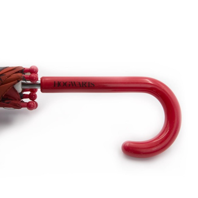 Czerwony parasol dziecięcy Harry Potter z logo HOGWARTS na rączce. Rączka o falistym kształcie w kolorze czerwonym, z kulistymi końcówkami. Parasol złożony, widok z boku, na białym tle.