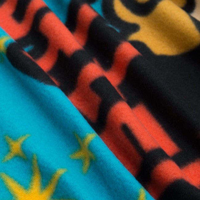 Kocyk dziecięcy 100x150 cm w kolorach niebieskim, czarnym i pomarańczowym, ozdobiony wzorami gwiazd oraz motywem z napisami. Widoczny w złożonej pozycji, z widoczną miękką fakturą materiału. Produkt przeznaczony dla dzieci.