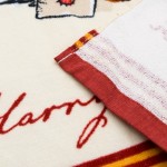 Ręcznik bawełniany dla dzieci w kolorze kremowym, z czerwonym obszyciem, prezentuje wzór z postacią Sowy Hedwigi oraz napisem Harry. Widok na detal obszycia i fakturę materiału, leżący rozłożony na płasko. Idealny do przedszkola.
