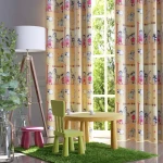 Dekoracyjna drukowana tkanina zasłona Baranek w odcieniach żółci z kolorowymi wzorami dziecięcych postaci i zwierząt. Tkanina wisząca na oknie w pokoju dziecięcym, z roślinnością w donicach i meblami w jasnych, pastelowych kolorach.