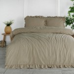 Komplet poszewek bawełnianych z falbanką w odcieniu szaro-beżowym, składający się z dwóch poduszek 40x40 cm. Ułożony na łóżku z materiałem o lekko wrinklowanej fakturze, z ozdobnym falbaniem oraz widocznymi poduszkami. W tle roślinność i drewniane meble.