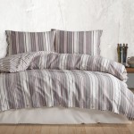 Pościel bawełniana 140x200 cm w poziome, klasyczne paski w odcieniach beżu, szarości i brązu. Rozłożona na łóżku, z wyraźnymi, dekoracyjnymi guzikami oraz poduszkami dopasowanymi do poszwy. Tło ciemne, fakturowane, zapewniające kontrast.