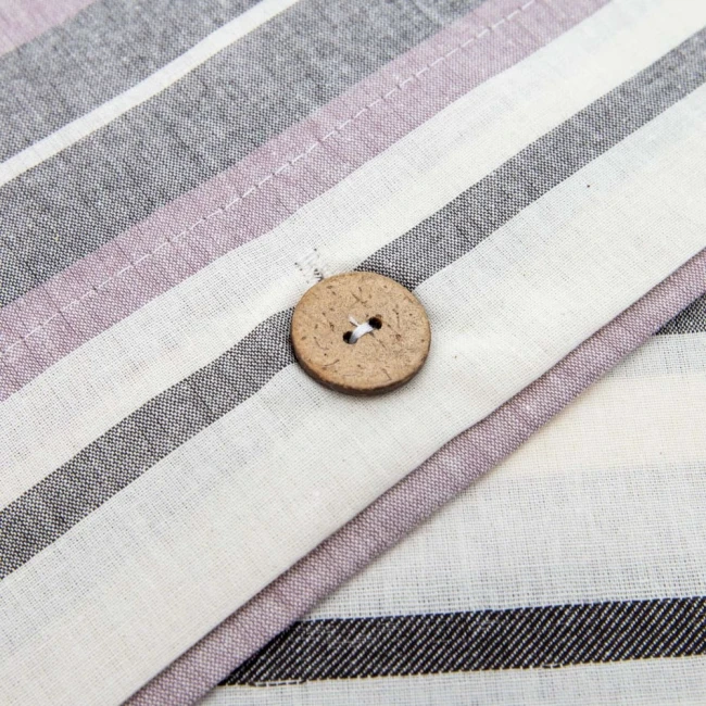Pościel bawełniana 140x200 w paski w odcieniach szarości, bieli i fioletu. Zbliżenie na detal z guzikiem z naturalnego drewna. Widok ukazuje strefę przy zamkniętej poszewce, z delikatnym wykończeniem na krawędziach.
