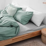 Prześcieradło flanelowe 160x210 cm, kolor jasny szary, na łóżku z poduszkami w odcieniu miętowym i białym. Złożone, z widoczną teksturą materiału na gładkim, ciemniejszym tle.