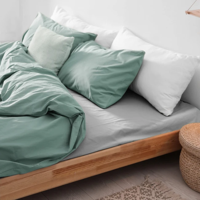 Prześcieradło flanelowe 160x210 cm, kolor jasny szary, na łóżku z poduszkami w odcieniu miętowym i białym. Złożone, z widoczną teksturą materiału na gładkim, ciemniejszym tle.