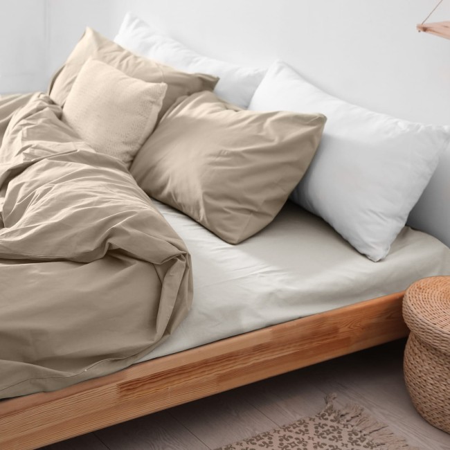 Prześcieradło flanelowe bez gumki w kolorze kremowym 180x210, leżące na łóżku, obok poduszki. Widać teksturę materiału oraz rozłożoną fakturę. Na łóżku znajdują się także białe poduszki oraz wiklinowy kosz w tle.