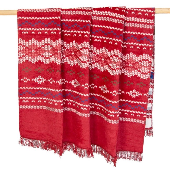 Koc bawełniany 150x200 cm w czerwonym kolorze z białymi, niebieskimi i zielonymi wzorami świątecznymi. Zakończony frędzlami, zawieszony na drewnianym wieszaku. Idealny do dekoracji wnętrz w okresie świątecznym.