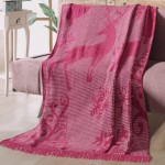 Koc bawełniany o wymiarach 150x200 cm w bordowym kolorze, z dekoracyjnym wzorem renifera i płatków śniegu. Leży na sofie, lekko zwinięty. Wykończony frędzlami, wykonany z teksturowanej tkaniny. Idealny na zimowe wieczory.