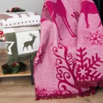 Koc bawełniany w kolorze bordowym, rozmiar 150x200 cm, z wzorem zimowym, w tym sylwetkami reniferów i śnieżynek. Produkt leży na stole, w otoczeniu dekoracji świątecznych. Widoczne frędzle na brzegach oraz struktura materiału.