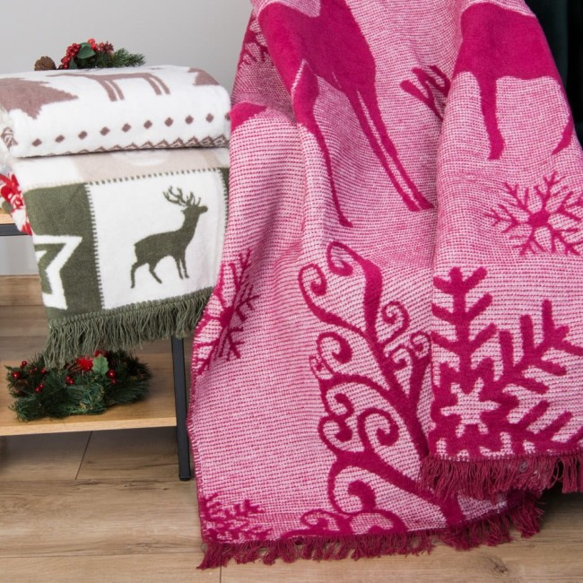 Koc bawełniany w kolorze bordowym, rozmiar 150x200 cm, z wzorem zimowym, w tym sylwetkami reniferów i śnieżynek. Produkt leży na stole, w otoczeniu dekoracji świątecznych. Widoczne frędzle na brzegach oraz struktura materiału.