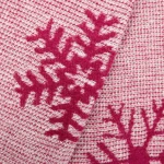 Koc bawełniany 150x200 cm w bordowym kolorze z białymi wzorami świątecznymi. Produkt leży na gładkiej powierzchni. Tekstura jest miękka, widoczne zdobienia w formie śnieżynek. Idealny do dekoracji wnętrz w okresie zimowym.