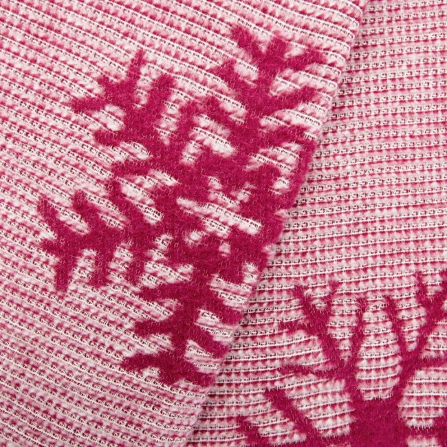 Koc bawełniany 150x200 cm w bordowym kolorze z białymi wzorami świątecznymi. Produkt leży na gładkiej powierzchni. Tekstura jest miękka, widoczne zdobienia w formie śnieżynek. Idealny do dekoracji wnętrz w okresie zimowym.