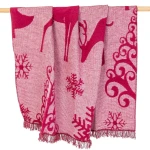 Koc bawełniany 150x200 cm w odcieniu bordowym z zimowymi motywami, w tym reniferami i płatkami śniegu. Produkt wiszący, z frędzlami na dolnej krawędzi, o teksturowanej powierzchni. Idealny na sezon świąteczny.