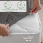 Prześcieradło jersey z elastanem w kolorze antracytowym, z gumką, idealne na materac o grubości 25 cm. Ujęcie z boku, ręka trzyma krawędź prześcieradła, ukazując jego elastyczność i dopasowanie. Na tle widoczne informacje o właściwościach materiału.