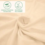 Prześcieradło jersey w kolorze beżowym, z elastanem, ukazujące gładką, elastyczną tkaninę o matowej strukturze. Widoczne znaki informacyjne: miękka tkanina w dotyku oraz delikatna dla skóry. Produkt rozłożony na płasko.