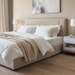 Białe prześcieradło jersey z elastanem z gumką w rozmiarze 180x200 leży na łóżku z jasnym, tapicerowanym wezgłowiem. Obok widoczny jest nocny stoliczek oraz lampka. Tło w neutralnych kolorach, podłoga drewniana.