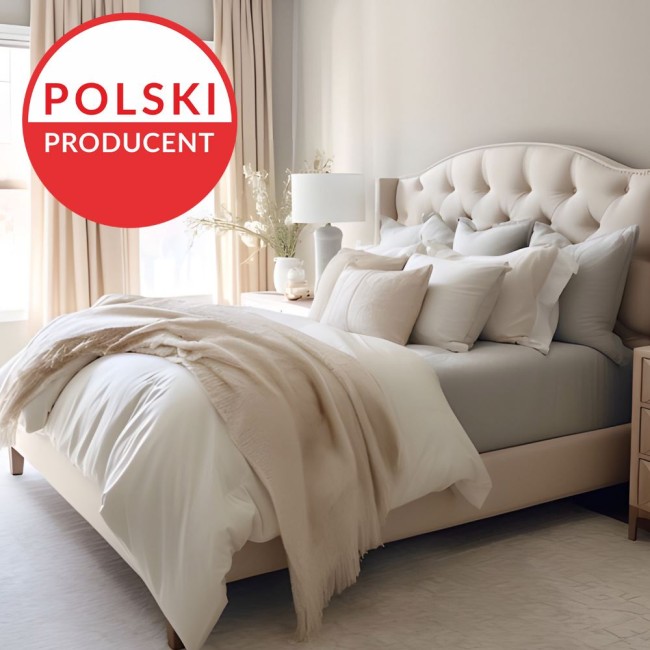 Prześcieradło jersey z elastanem w kolorze białym, rozmiar 180x200, leżące na łóżku z jasną pościelą. Widoczna tekstura materiału, która zapewnia elastyczność. W tle elementy wystroju sypialni, takie jak połyskująca lampa i dekoracyjne poduszki.