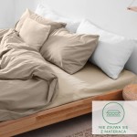 Prześcieradło flanelowe z gumką w kolorze jasno beżowym, rozłożone na materacu. Widoczne wysokie poduszki w odcieniach beżu i bieli, na naturalnym drewnianym łóżku. W rogu etykieta informująca o gumce zapobiegającej przesuwaniu.