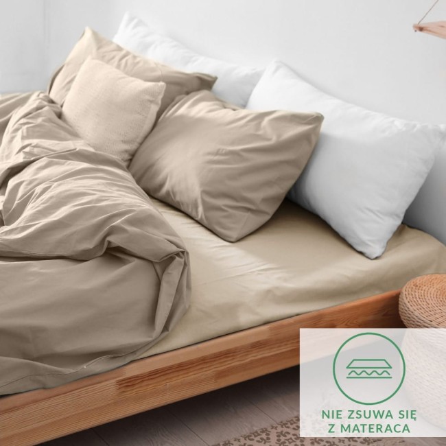 Prześcieradło flanelowe z gumką 90x200 w kolorze jasno beżowym leży na łóżku, otulające materac. Widoczne są poduszki w białym kolorze, a na tkaninie delikatna faktura. Na dolnej części zdjęcia znajduje się logo z informacją, że nie zsuwa się z materaca.