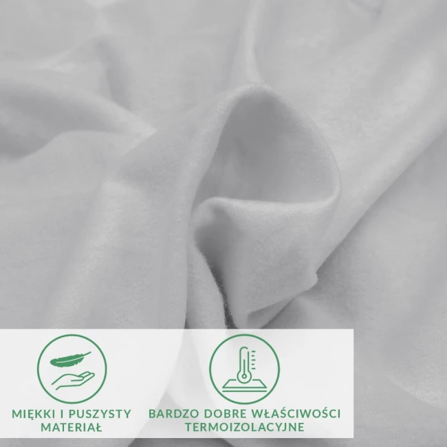 Prześcieradło flanelowe z gumką w jasnoszarym kolorze, wykonane z miękkiego materiału. Produkt leży na gładkiej powierzchni, ukazując delikatną fakturę tkaniny. Widoczne są napisy dotyczące właściwości materiału, z jasnym podkreśleniem cech termicznych.