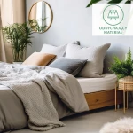 Prześcieradło flanelowe z gumką 140x200 w kolorze szarym, wykonane z materiału o gramaturze 160 g/m2, nałożone na łóżko. W tle widoczne jasne poduszki w odcieniach szarości i pomarańczy oraz rośliny w donicach. Przytulna aranżacja sypialni.