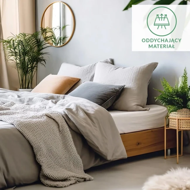 Prześcieradło flanelowe z gumką 140x200 w kolorze szarym, wykonane z materiału o gramaturze 160 g/m2, nałożone na łóżko. W tle widoczne jasne poduszki w odcieniach szarości i pomarańczy oraz rośliny w donicach. Przytulna aranżacja sypialni.