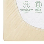Prześcieradło jersey z gumką 180x200 w kolorze kremowym, widoczne w zbliżeniu na narożnik. Zawiera elastyczną gumę obwodową, a na materiale widoczne napisy dotyczące jego właściwości. Struktura tkaniny jest gładka i matowa.