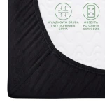 Czarne prześcieradło jersey z gumką 180x200, rozłożone na białym materacu. Zbliżenie na obszycie, z widoczną grubością i wytrzymałością gumy. W tle wytłoczenia na powierzchni materaca, wyraźne napisy dotyczące cech produktu.