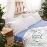 Prześcieradło jersey z gumką 60x120 w kolorze niebieskim, leżące na łóżku. Jest dopasowane do materaca, z widoczną gładką fakturą.